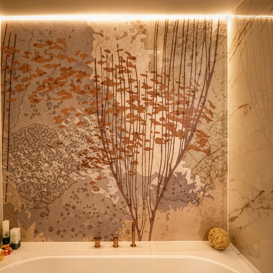 Ein Badezimmer mit einer großen Wandmalerei eines Baumes mit braunen Blättern. Eine Badewanne mit weißer Porzellanoberfläche ist unter der Wandmalerei platziert. Ein Licht beleuchtet die Wand und wirft einen warmen Schein auf die Wand.