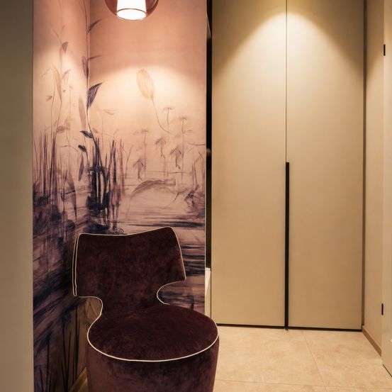 Ein modernes Zimmer mit einer rosa Wand, die künstlerische Pflanzen zeigt. Ein dunkellila Stuhl steht in der Ecke. Daneben befindet sich eine weiße Schiebetür.