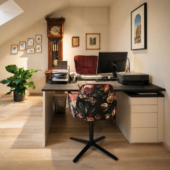 Ein Zimmer mit einem Schreibtisch, einem Computer, einem Drucker und einem Stuhl. Im Zimmer stehen ein Topf mit Pflanzen und eine Großuhr. An der Wand hängen auch Bilderrahmen.