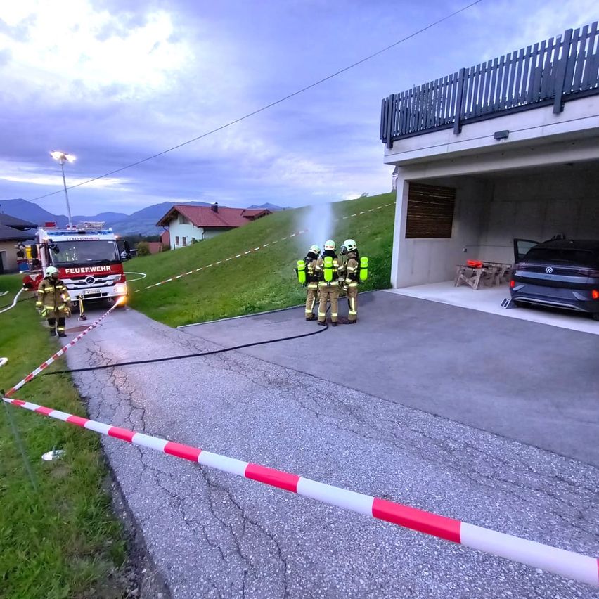 Feuerwehrleute verwenden einen Schlauch, um ein Feuer in der Nähe eines Hauses zu löschen. Der Feuerwehrwagen ist in der Nähe geparkt.