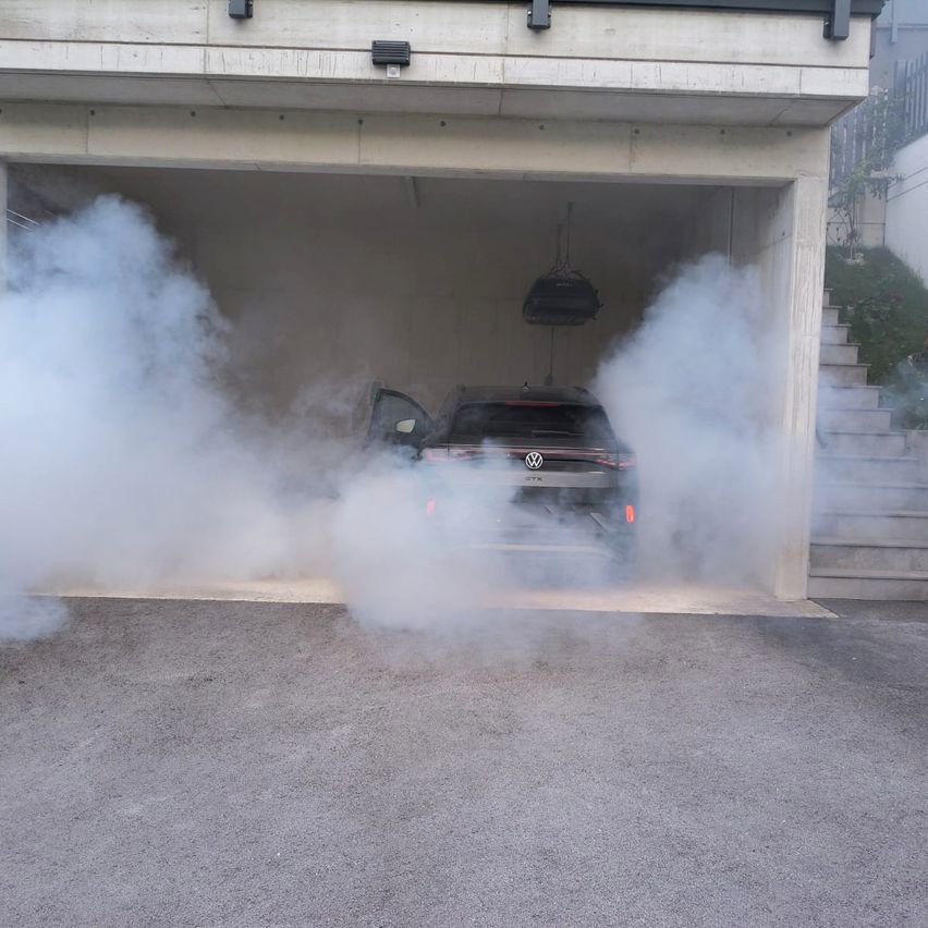 Ein Auto mit offener Tür lässt Rauch aus dem Auspuff in einer Garage austreten.