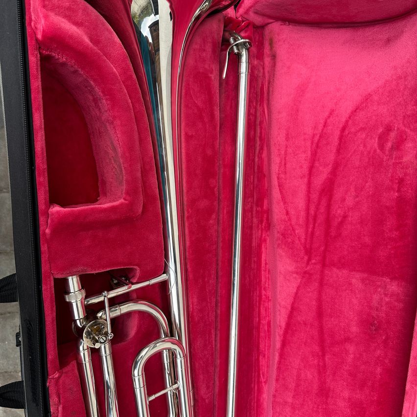 Ein Posaune befindet sich in einem rot samtgefütterten Etui. Das Etui ist geöffnet und zeigt die polierte silberne Posaune und ihre Rohre.