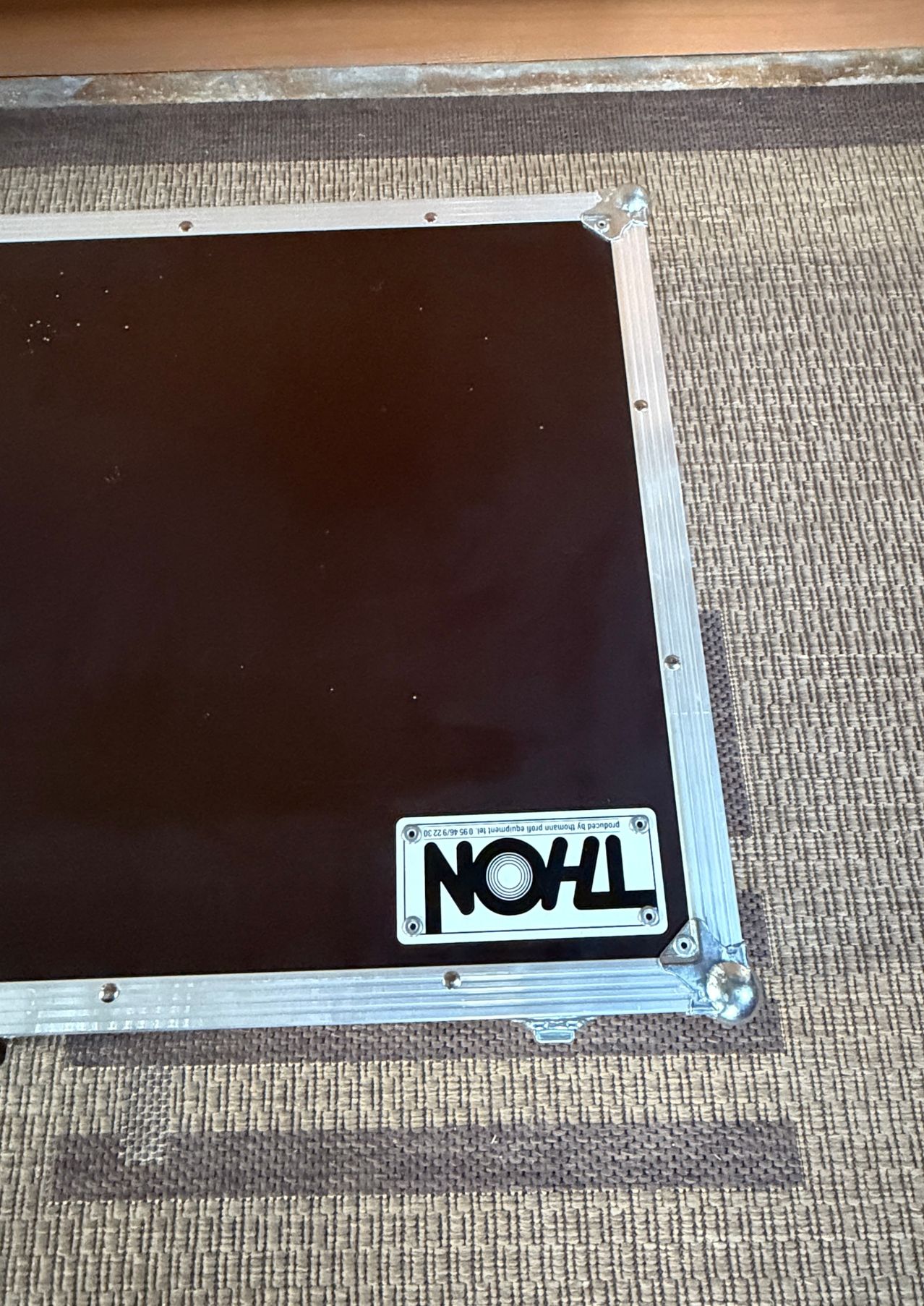 Ein schwarzer Koffer mit silbernem Rahmen und einem weißen Aufkleber mit der Aufschrift NOHL auf einer strukturierten Oberfläche.