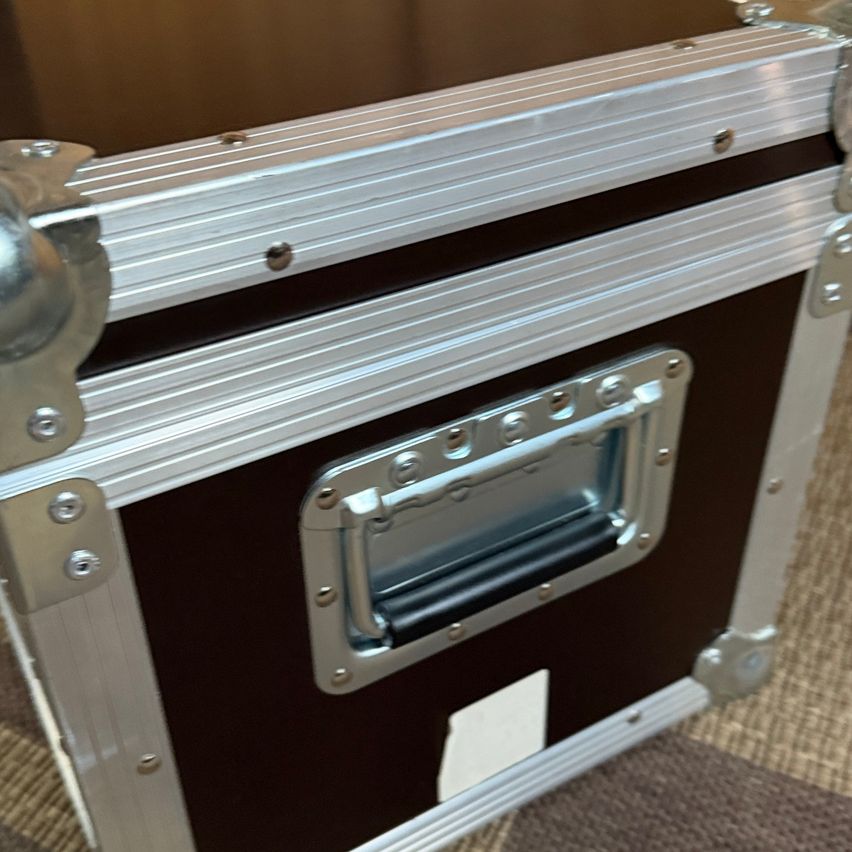 Eine Nahaufnahme einer metallischen und braunen Aufbewahrungsbox mit silbernem Griff und Verschluss, die auf einem beigen Teppich liegt.