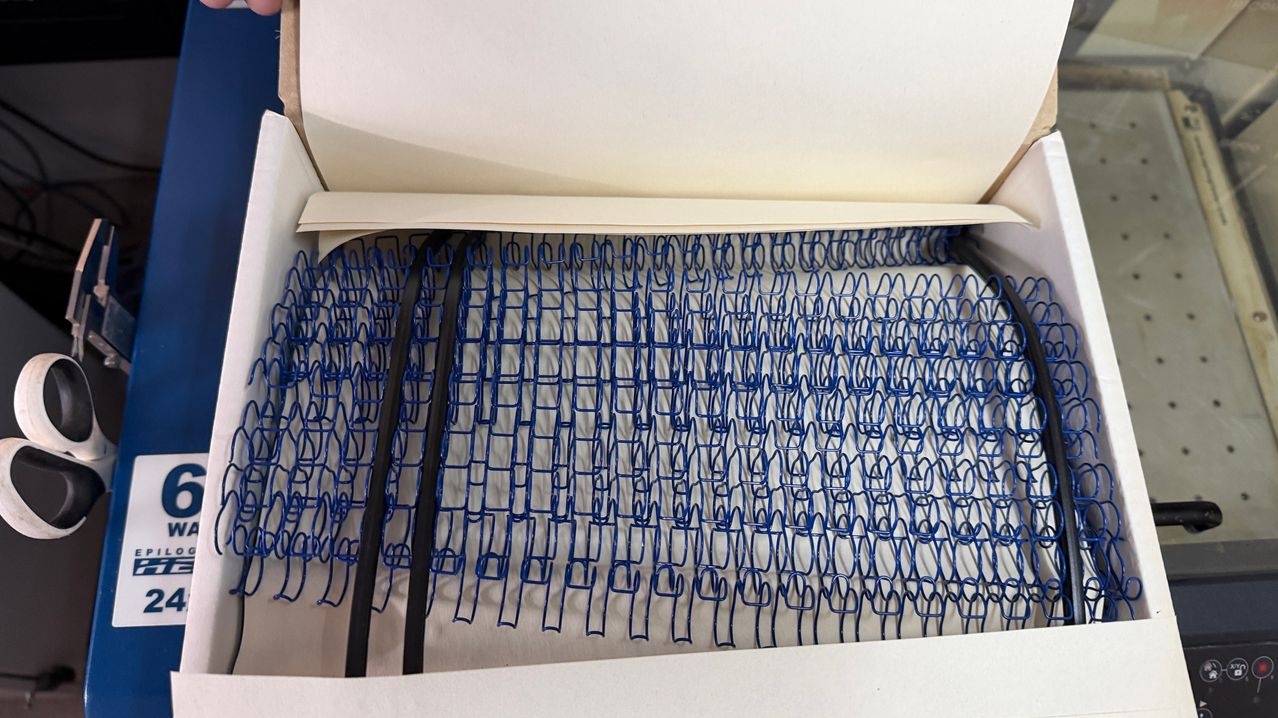 Eine offene Box gefüllt mit zahlreichen blauen Spiralen, möglicherweise eine Spiralfeder, auf einer weißen Oberfläche liegend.