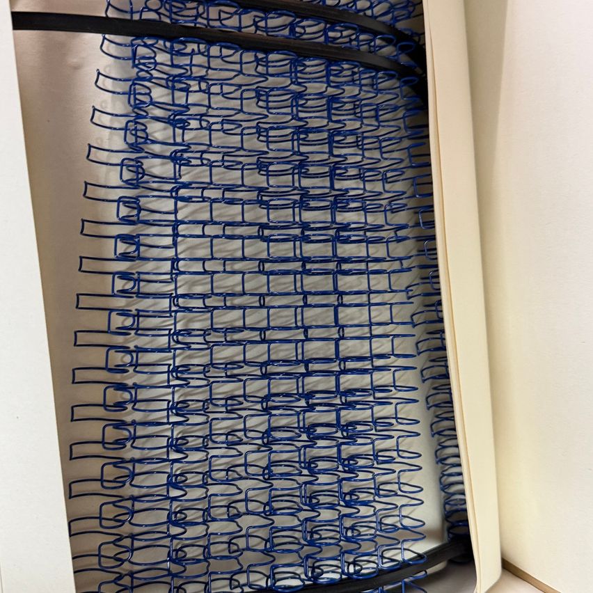 Ein Nahaufnahme einer blauen Metallspiralfeder, ordentlich in einem Rastermuster angeordnet, wird auf einem weißen Hintergrund angezeigt.