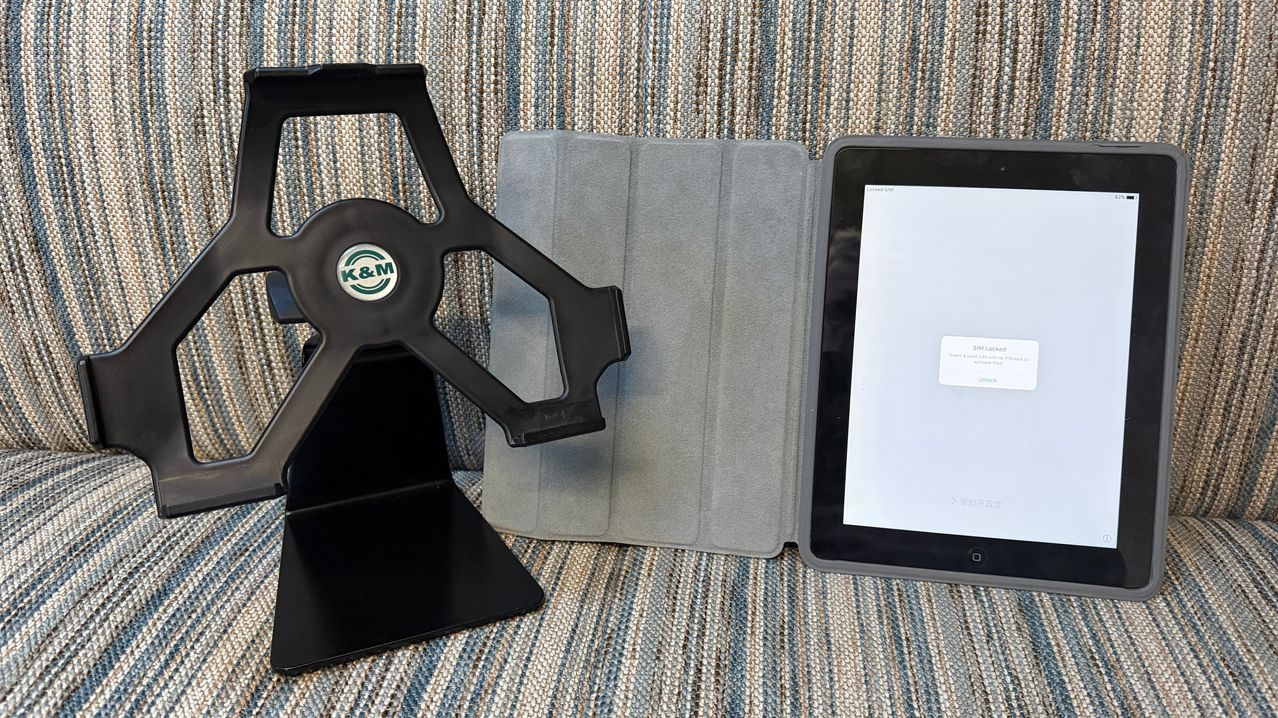 Ein Tablet auf einem Ständer mit einer Hülle daneben. Das Tablet hat eine Nachricht über SIM-Sperre. Der Ständer und die Hülle sind schwarz.