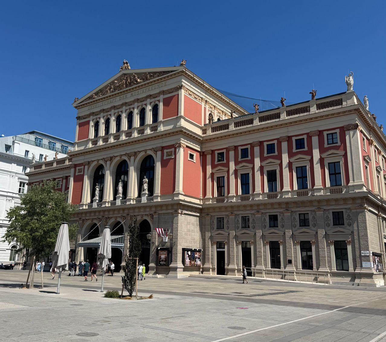 Ein großes rotes und weißes Gebäude mit Statuen und Säulen vor einem klaren blauen Himmel.