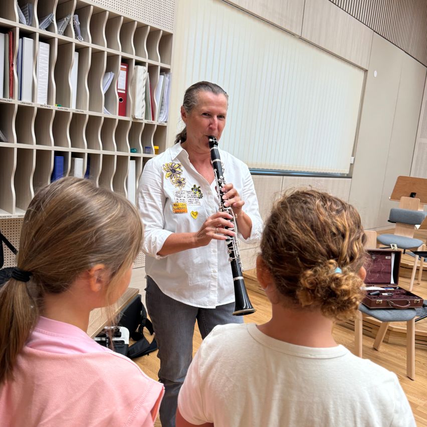 Eine Frau unterrichtet zwei junge Mädchen, wie sie Klarinette spielen, in einem Klassenzimmer.