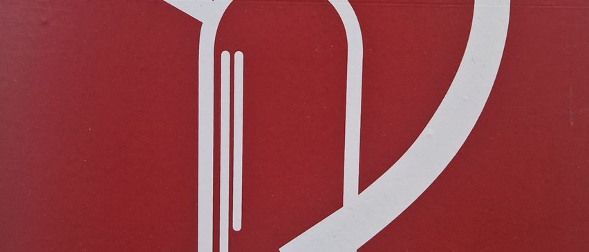 Ein rotes Schild mit einem weißen Feuerwehr-Spritzen-Symbol darauf. Die Feuerlöscher-Ikone ist stilisiert mit einem zylindrischen Körper, einem Düsenrohr und einem Griff dargestellt.