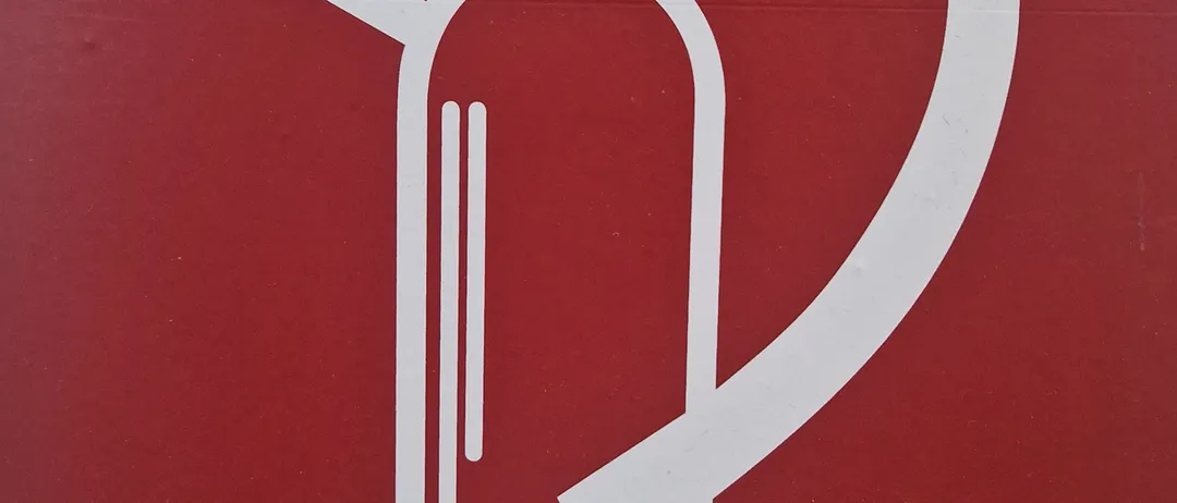 Ein rotes Schild mit einem weißen Feuerwehr-Spritzen-Symbol darauf. Die Feuerlöscher-Ikone ist stilisiert mit einem zylindrischen Körper, einem Düsenrohr und einem Griff dargestellt.
