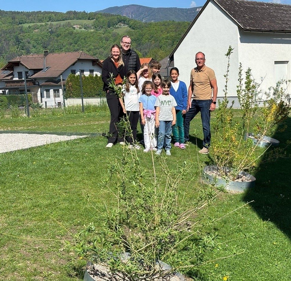 Eine Familie mit zwei Erwachsenen und fünf Kindern steht in einem Garten mit Pflanzen und Bäumen im Hintergrund.
