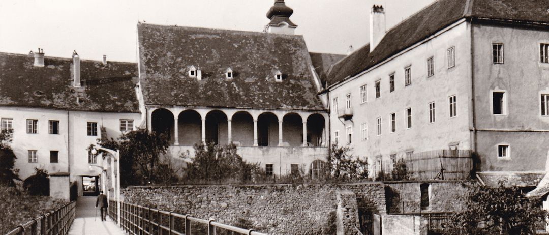 Ein Schwarz-Weiß-Foto der Clarissenkirche mit Steg, einem historischen Gebäude mit Steinmauer und Zaun, mit einem Turm und vielen Fenstern.