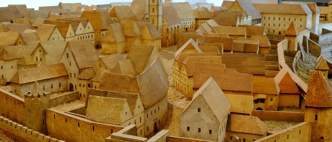 Ein detailliertes Holzmodell einer alten Stadt mit mehreren Gebäuden, Türmen und einer Burg. Die Gebäude sind in verschiedenen Größen und Stilen, einige mit komplizierten Details.