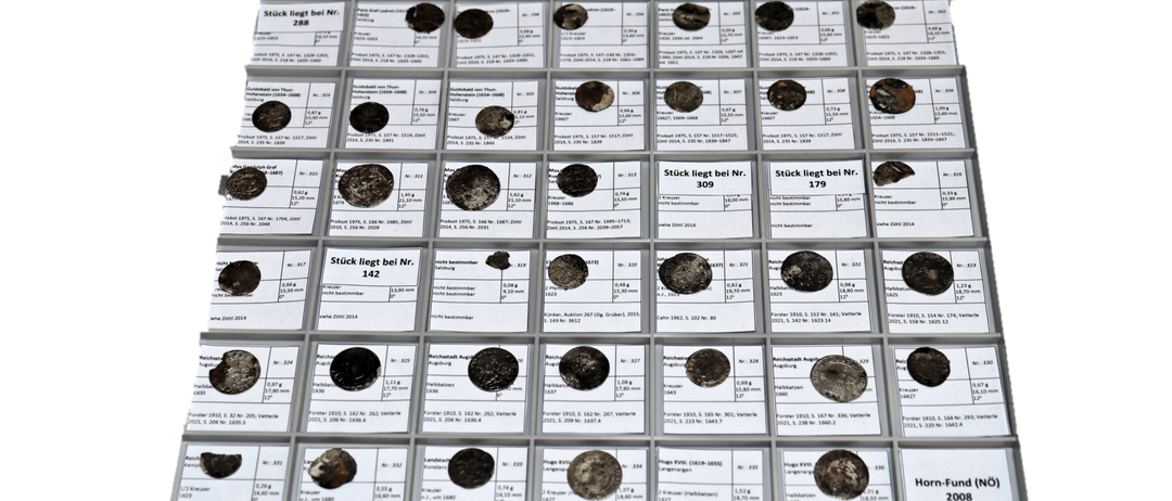 Eine Sammlung von Münzen, die in einem Rasterformat angeordnet ist, jede mit einem Etikett und einer Identifikationsnummer. Jede Münze hat eine begleitende Beschreibung ihres Produktionsjahres und Gewichts. Die Münzen sind in Reihen und Spalten angeordnet.