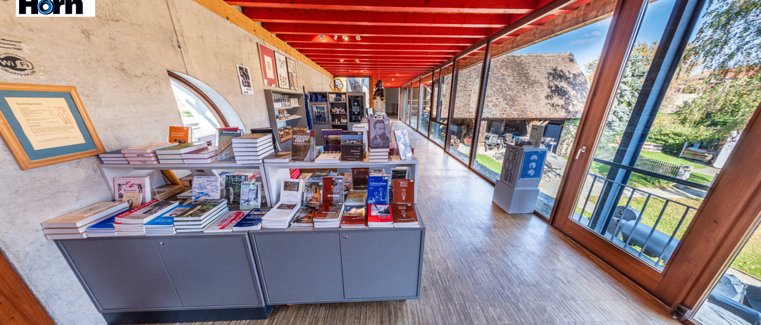 Ein Buchladen mit roter Decke, Holzböden und einer Vielzahl von Büchern zur Schau. Die Regale sind mit Büchern gefüllt und es hängen Bilderrahmen an der Wand.