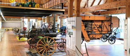 An indoor museum exhibit featuring a collection of vintage vehicles, including a tractor, steam engine, and horse-drawn carriages, displayed on a tiled floor under wooden beams.