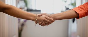 Zwei Personen schütteln sich in einem Büro die Hände. Sie tragen beide Schmuck.