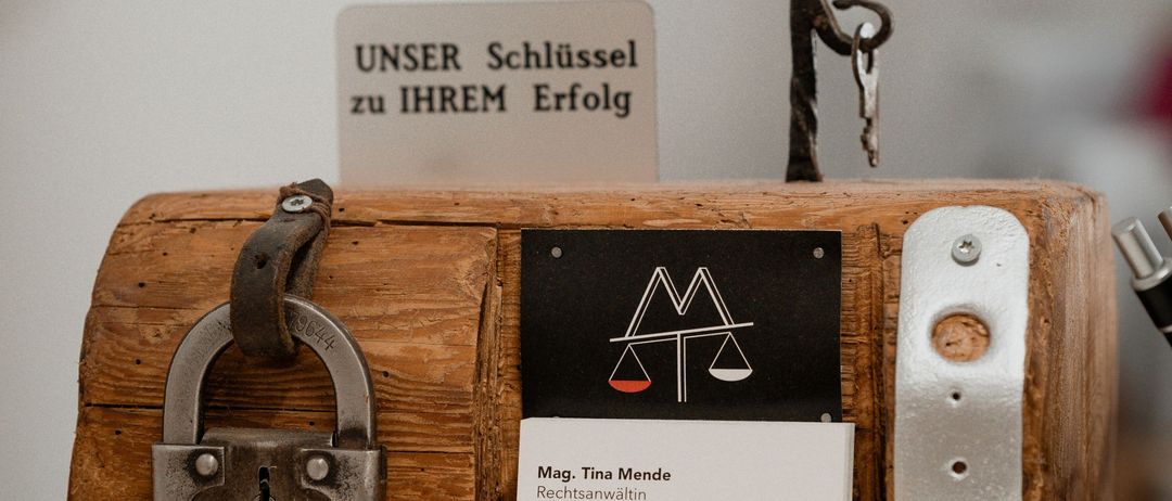 Eine Holzkiste mit einem Schloss und Kartenhalter. Die Karte zeigt 'Mag. Tina Mende Rechtsanwaltin'. Ein Vorhängeschloss ist an der linken Seite befestigt.
