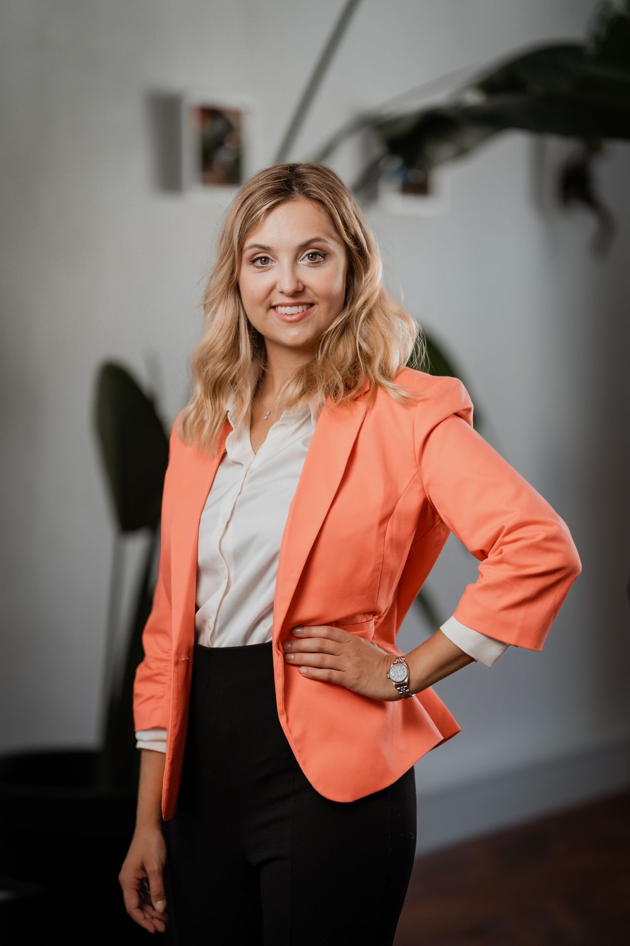 A smiling woman with blonde hair is standing and posing for a photograph. She is wearing a peach blazer and black skirt.