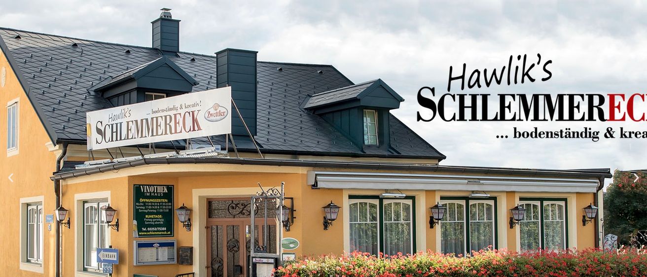 Ein gelbes Gebäude mit schwarzem Dach und einem Schild mit der Aufschrift 'Hav Schreck'. Es verfügt über mehrere Fenster, Lampen und einen Zaun mit roten Blumen. In der Nähe des Eingangs befindet sich ein Schild.