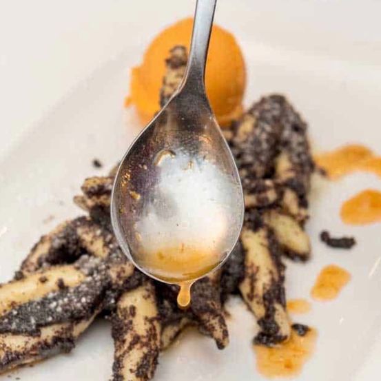 Ein Löffel mit Sirup über einem Teller mit frittierten Bananen mit einem Hauch von Orange auf der Seite.