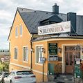 Ein Gebäude mit schwarzem Dach und einem Schild, das 'Zwetller Emmereck' steht. Das Gebäude hat eine gelbe Fassade mit Fenstern und einem Holzzaun mit roten Blumen.