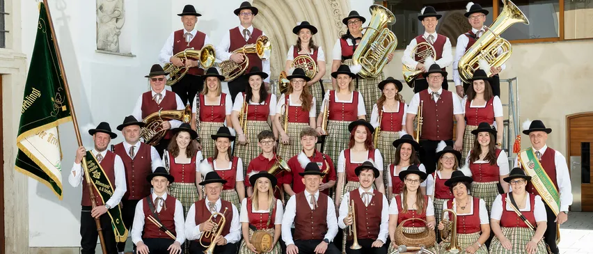Ein Blasorchester in traditioneller Kleidung posiert 2023 für ein Gruppenfoto vor einem Bogengebäude.