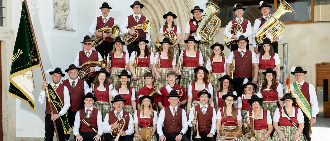 Ein Blasorchester in traditioneller Kleidung posiert 2023 für ein Gruppenfoto vor einem Bogengebäude.