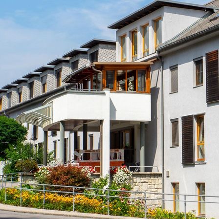 Eine Reihe weißer Häuser mit Holzbalkonen und Fenstern. Vor einem der Häuser steht ein roter Feuerwehrwagen.