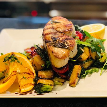 Ein Teller mit gegrillten Jakobsmuscheln, Zitronenscheiben und einer Mischung aus geröstetem Gemüse wie Zucchini, Brokkoli und Tomaten.