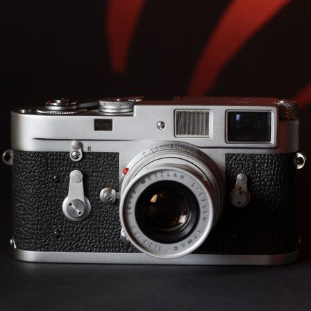 Eine Vintage Leica Kamera wird auf einem schwarzen Hintergrund mit roten Streifen gezeigt. Die Kamera hat einen schwarzen und silbernen Korpus mit einer silbernen Linse.