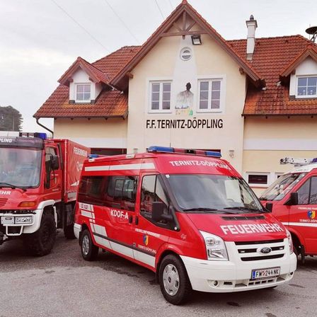 Drei rote Feuerwehrfahrzeuge sind vor dem Gebäude der F.F. Ternitz-Döpling geparkt, wobei der mittlere Van mit 'FEUERWEHR' und 'KDOF-A' an seiner Seite gekennzeichnet ist.