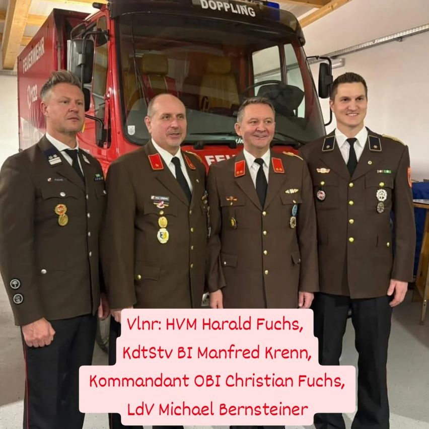 Vier Männer in Militäruniformen stehen vor einem roten Feuerwehrauto. Sie lächeln und posieren für ein Foto. Die Namen der Personen sind auf dem Bild vermerkt.