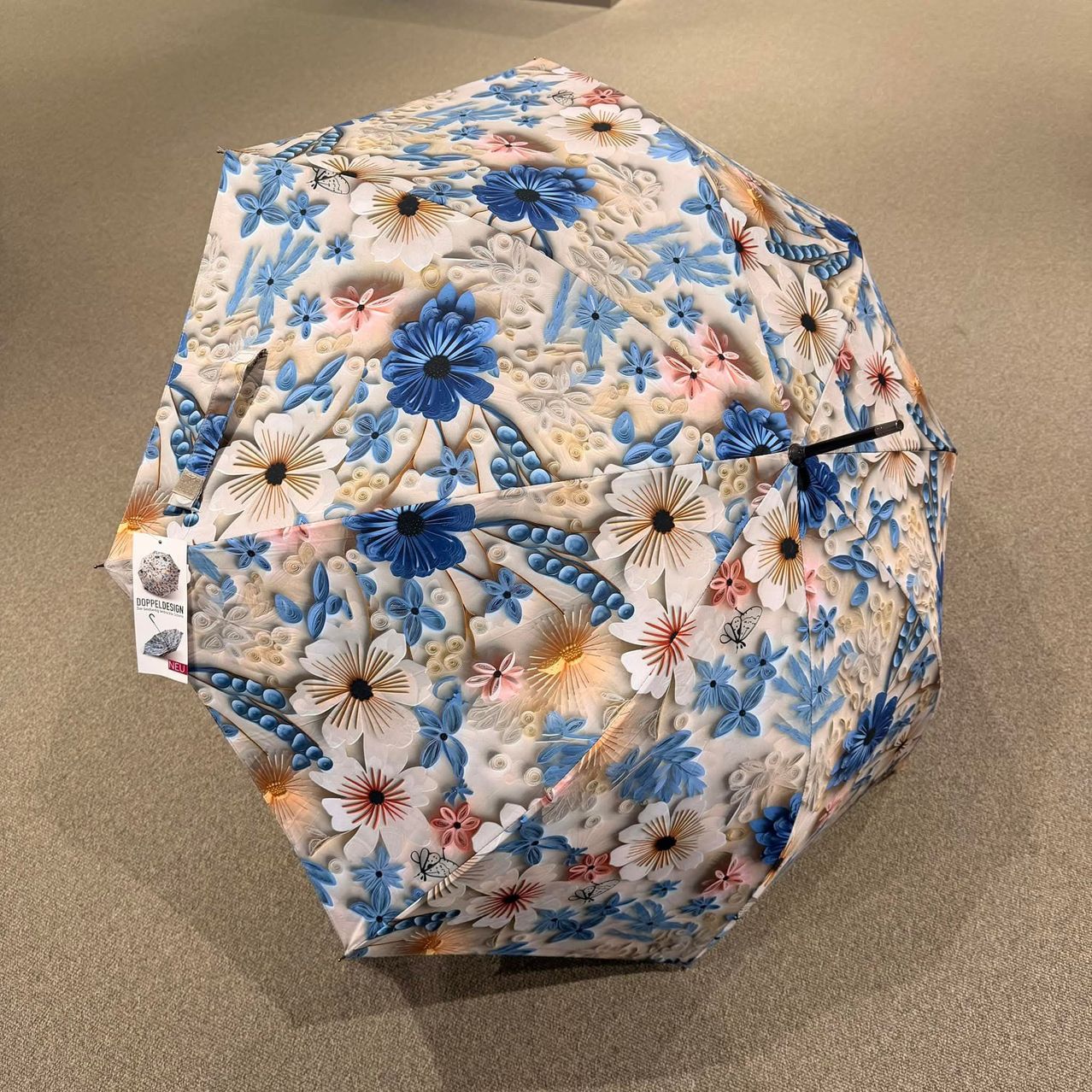 Ein geschlossener blau-weißer Blumenschirm auf einem beigen Teppich mit einem weißen Etikett.