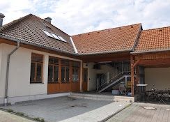 Ein Wohnhaus mit einem gefliesten Dach und Glasfenstern, mit einer Treppe zum Eingang. Die Vorderseite hat eine Einfahrt, an der ein Fahrrad geparkt ist.