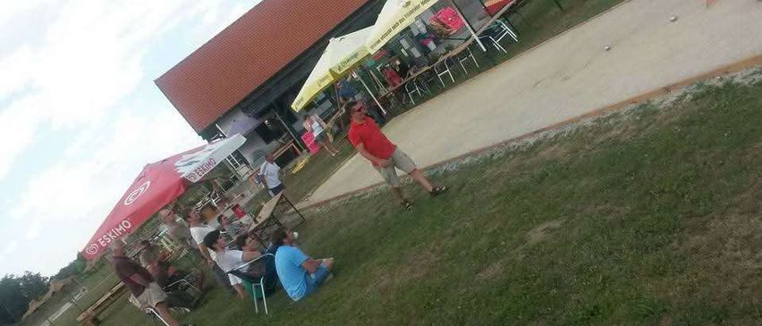 Eine Gruppe von Menschen sitzt unter Regenschirmen an einem Tisch in einem Park. Ein Mann steht im Gras.