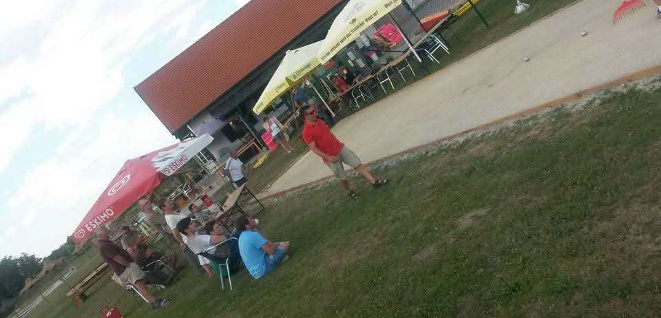 Eine Gruppe von Menschen sitzt unter Regenschirmen an einem Tisch in einem Park. Ein Mann steht im Gras.