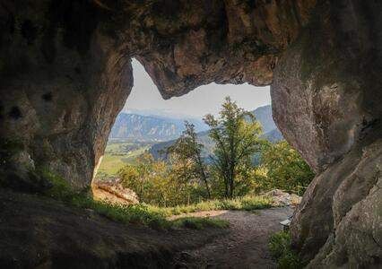 Blick aus einer Höhle mit einem Pfad, der zu einem Tal und Bergen in der Ferne führt.