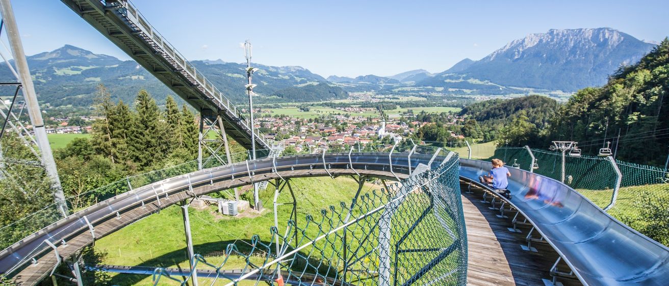 Eine Person fährt auf einer sonnigen Tag eine Achterbahn mit Bergen und einer Stadt im Hintergrund.