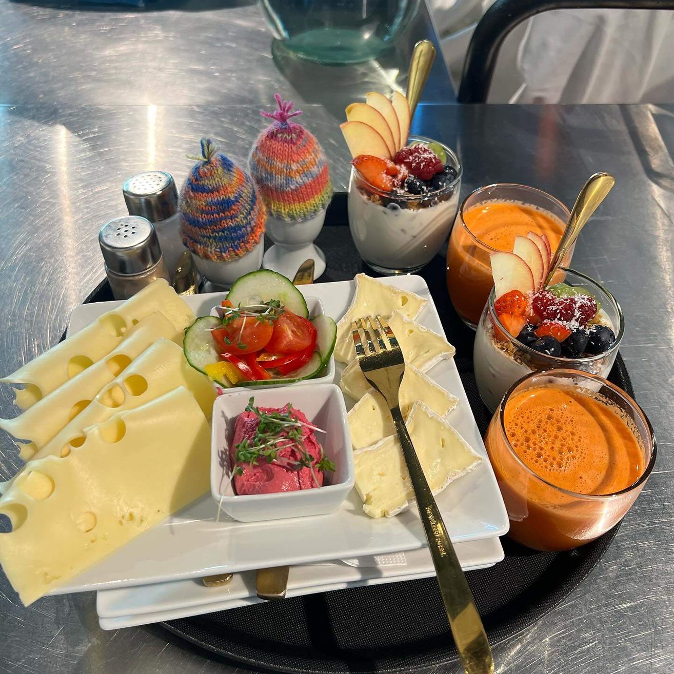 Ein Tablett mit Käse, Früchten, einer Gabel und einem Messer. Zwei Salz- und Pfefferstreuer und ein Glas Saft.