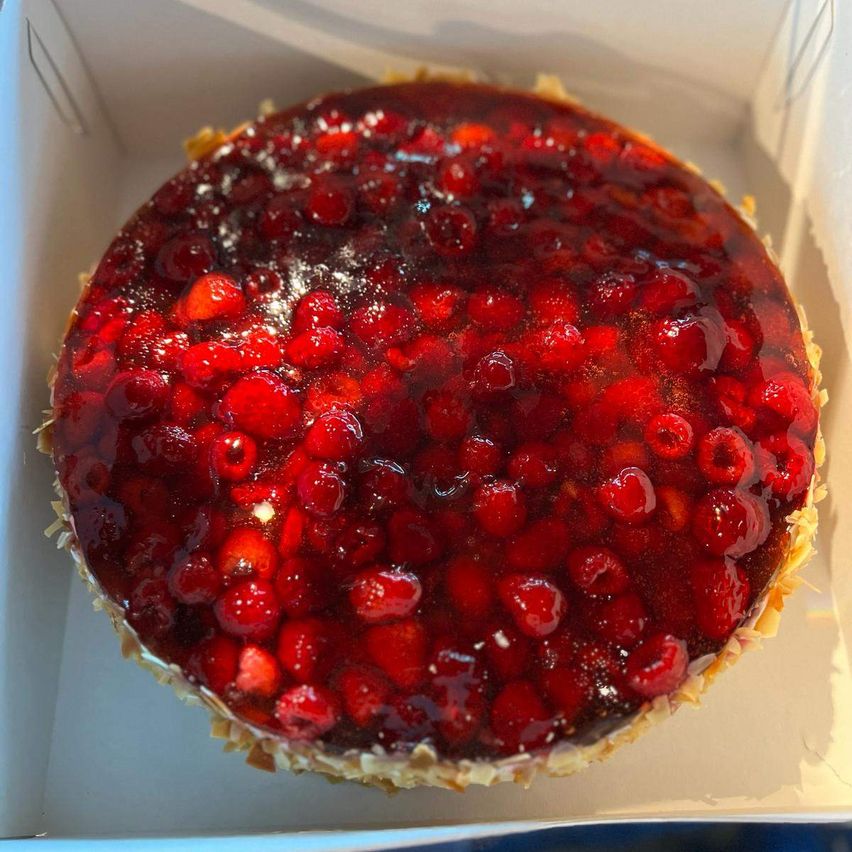 Ein runder Kuchen mit roter Beerenfüllung steht in einer weißen Schachtel. Die Beeren scheinen eine Mischung aus Himbeeren und Erdbeeren zu sein.