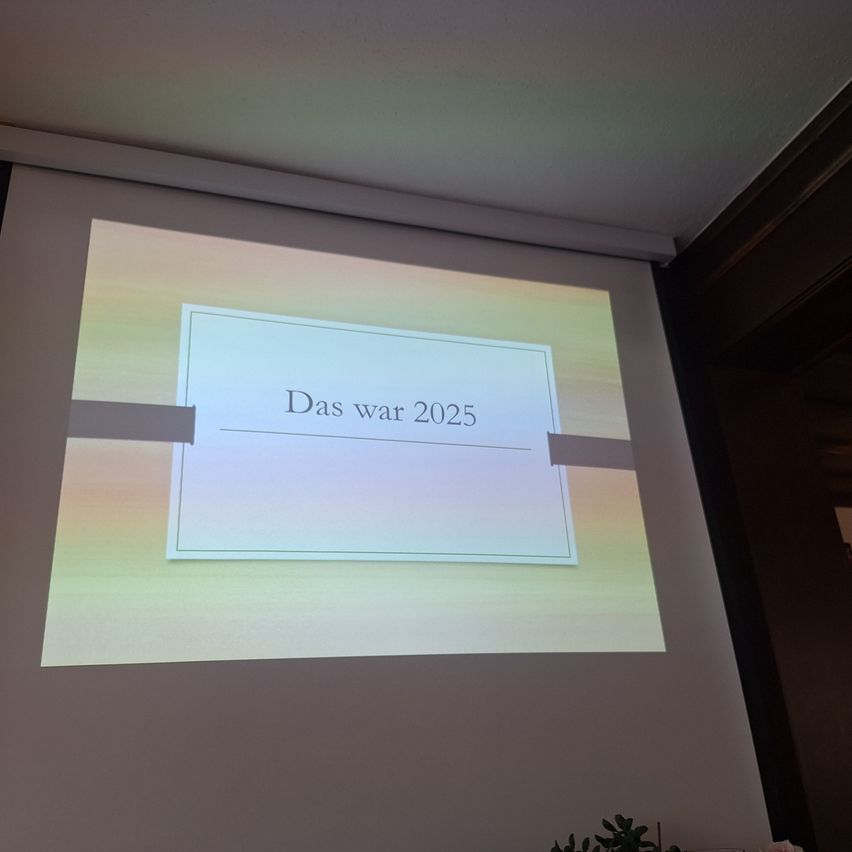 A projection screen displays a slide with the words 'Das war 2025' in white on a gradient background of green and yellow.
