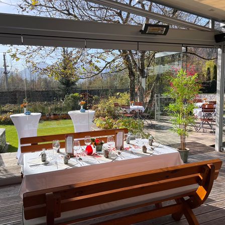 Eine Holzbank mit einem Tisch für eine Mahlzeit, umgeben von einer Glaswand, die einen Garten und einen Baum zeigt.