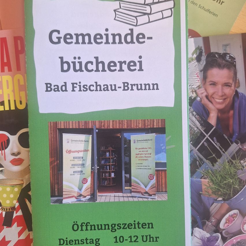 Ein grünes Poster mit weißem Text, das eine Gemeindebücherei in Bad Fischau-Brunn ankündigt. Die Öffnungszeiten sind in deutscher Sprache angegeben. Rechts ist eine lächelnde Frau abgebildet.