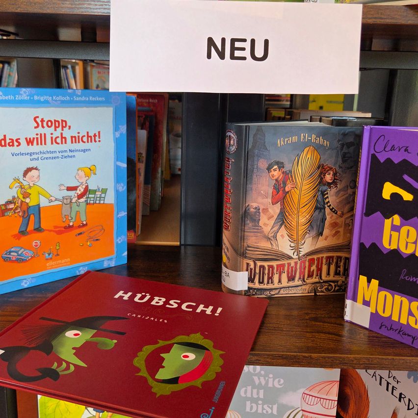 Ein Holzregal zeigt mehrere Kinderbücher, darunter eines mit dem Titel 'Stopp, das will ich nicht!' mit einem bunten Cover. Ein weißes Schild über den Büchern steht 'NEU'.