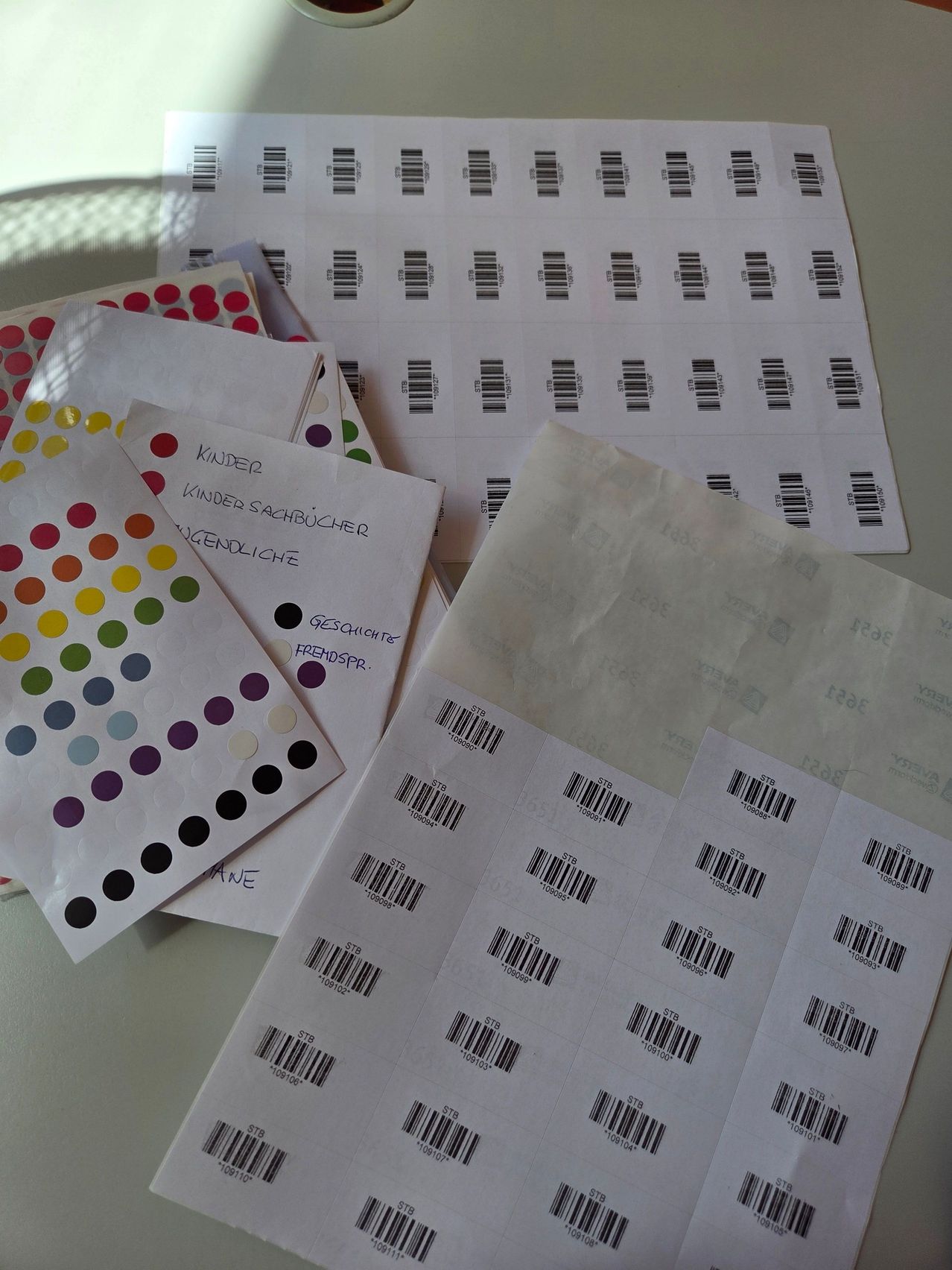 Eine Sammlung verschiedener Papiere mit Barcodes und handgeschriebenen Notizen, darunter eines mit bunten Punkten, auf einer weißen Oberfläche platziert.