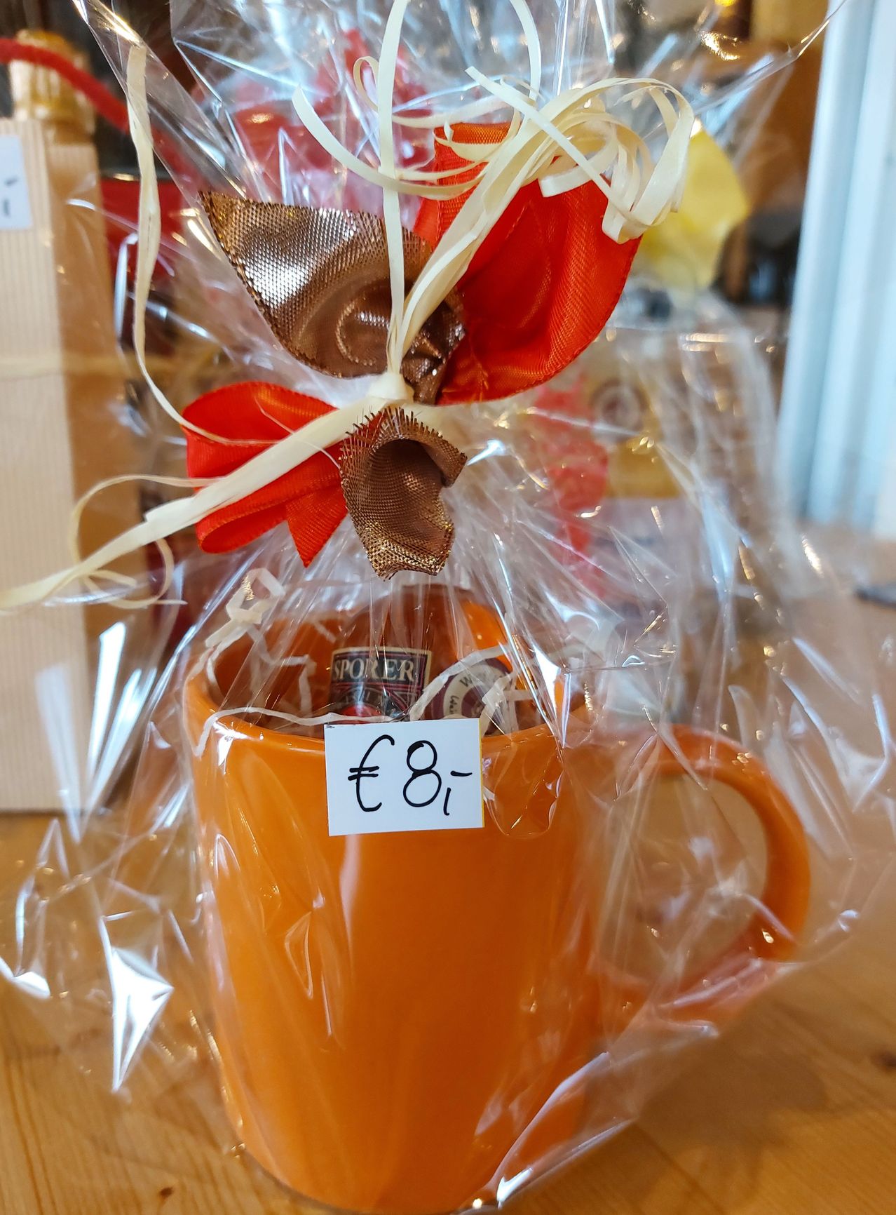 Ein orangefarbener Becher mit Plastikhülle und Schleife, beschriftet mit '€8'. Der Becher enthält eine Flasche Poker-Chips.