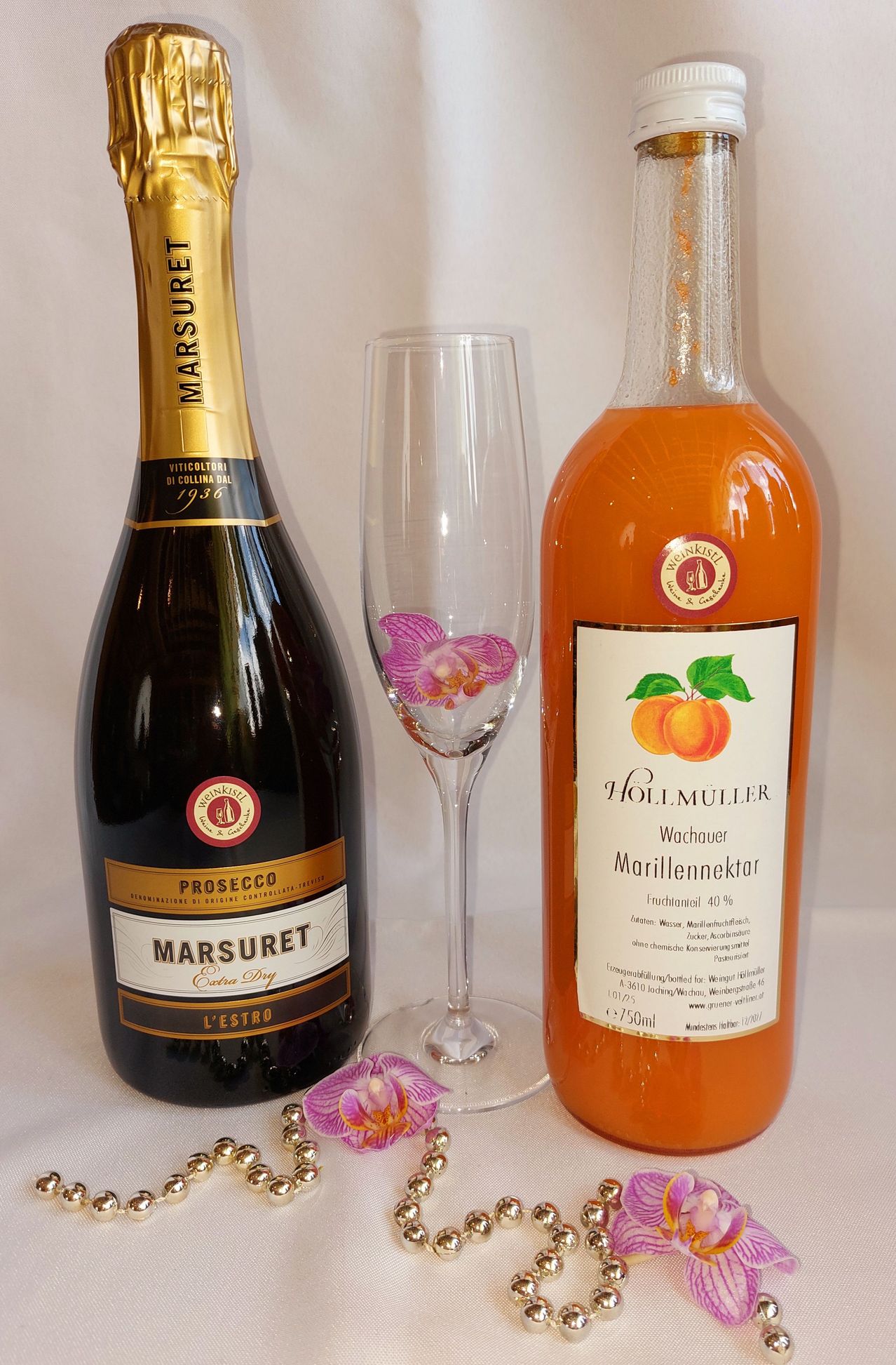 A bottle of Prosecco, a wine glass with a pink flower design, and a bottle of Hollmuller Wachauer Marillennektar.