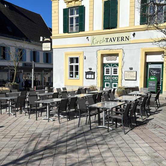 Eine Außensitzfläche mit Tischen und Stühlen vor einem Gebäude namens Kirch Tavern. Das Gebäude hat grüne Fensterläden und ein Schild über dem Eingang.